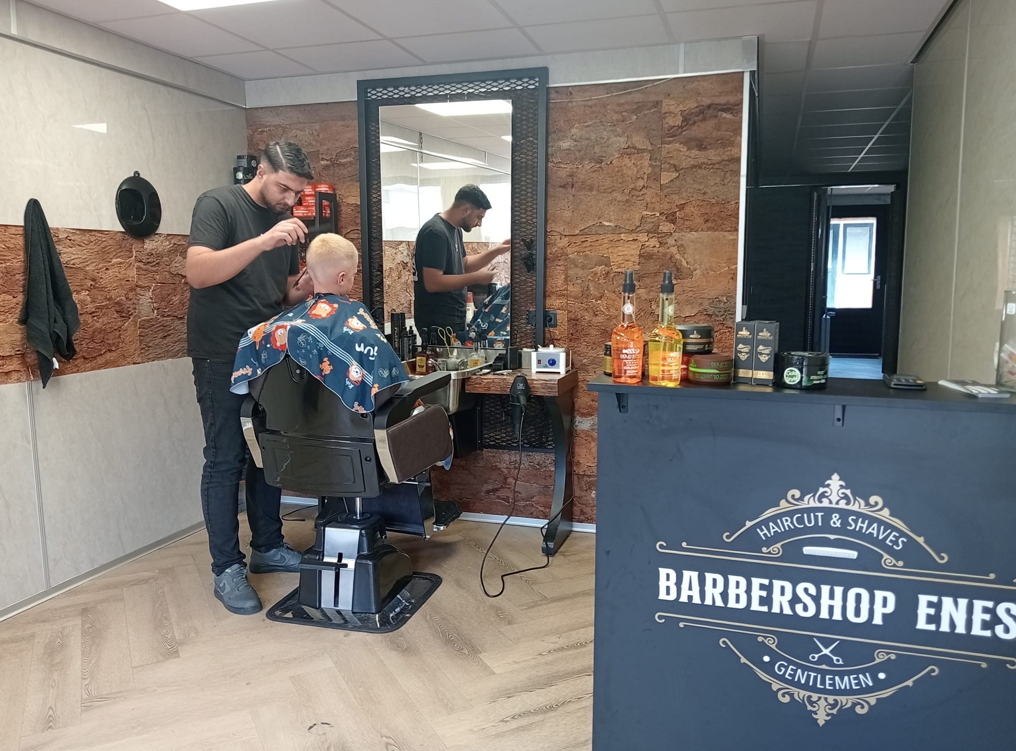 De zaak van binnen: Enes aan het werk bij de spiegel, vooraan de balie met Barbershop Enes, Haircut and Shaves, Gentlemen